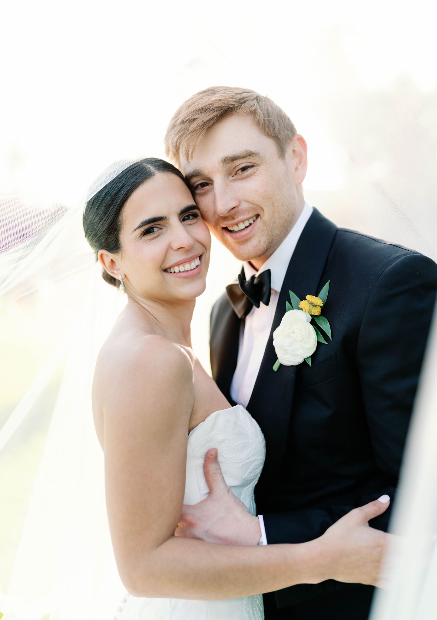 Ashley and Luke smiling together under her veil in soft golden light