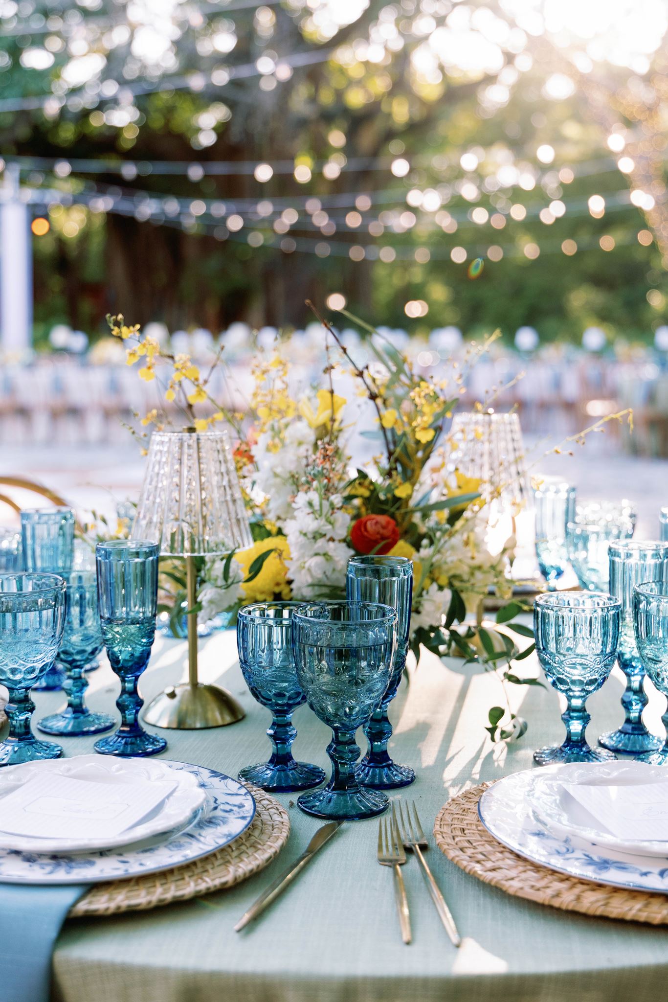 Reception table with blue goblets, woven chargers and yellow florals
