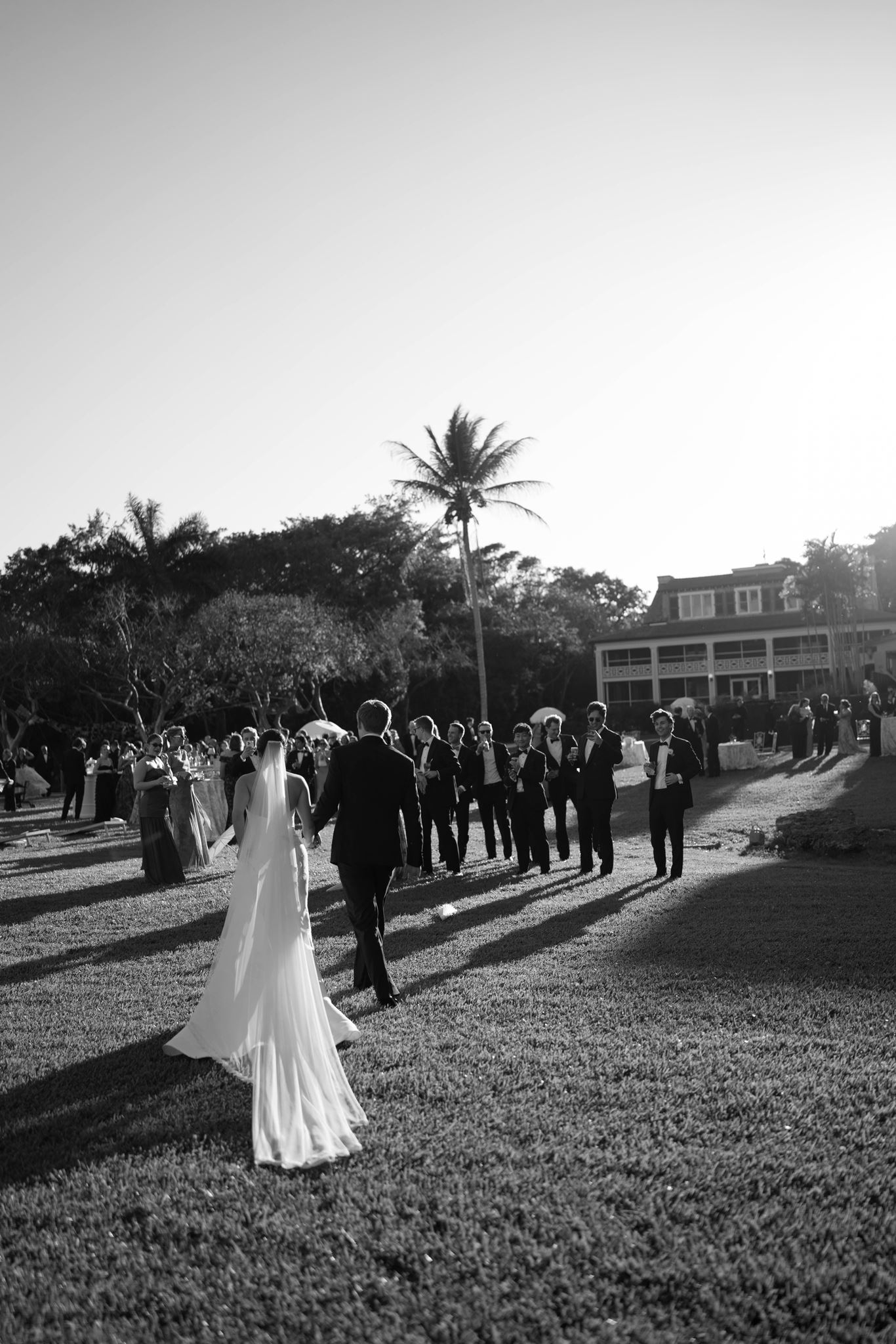 Ashley walking across the lawn toward guests at sunset in black and white