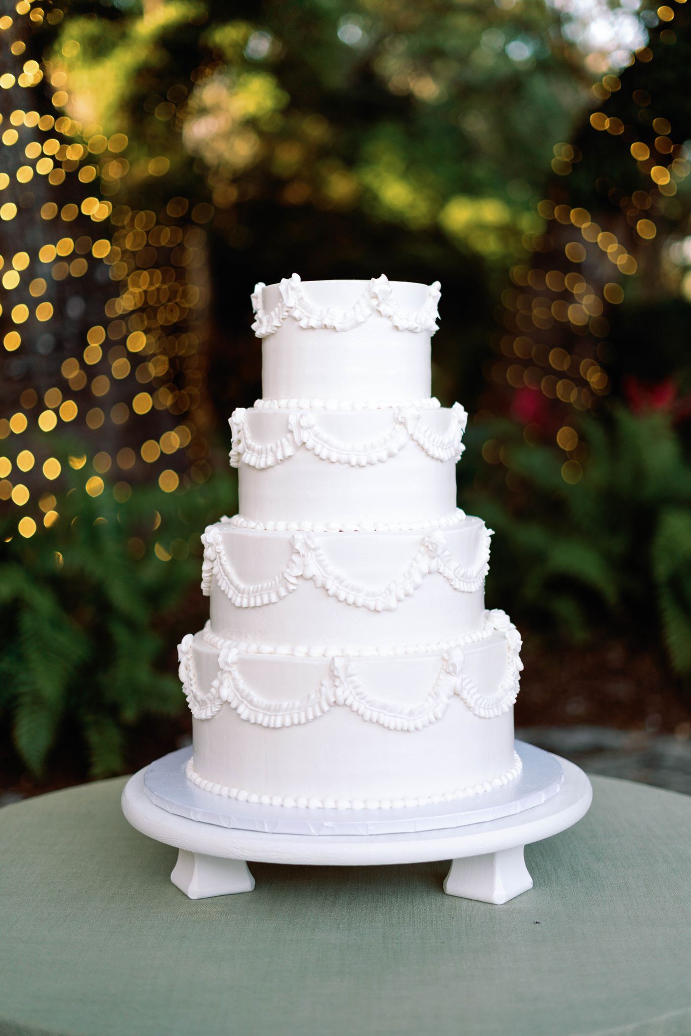 White wedding cake with piped details in front of string lights