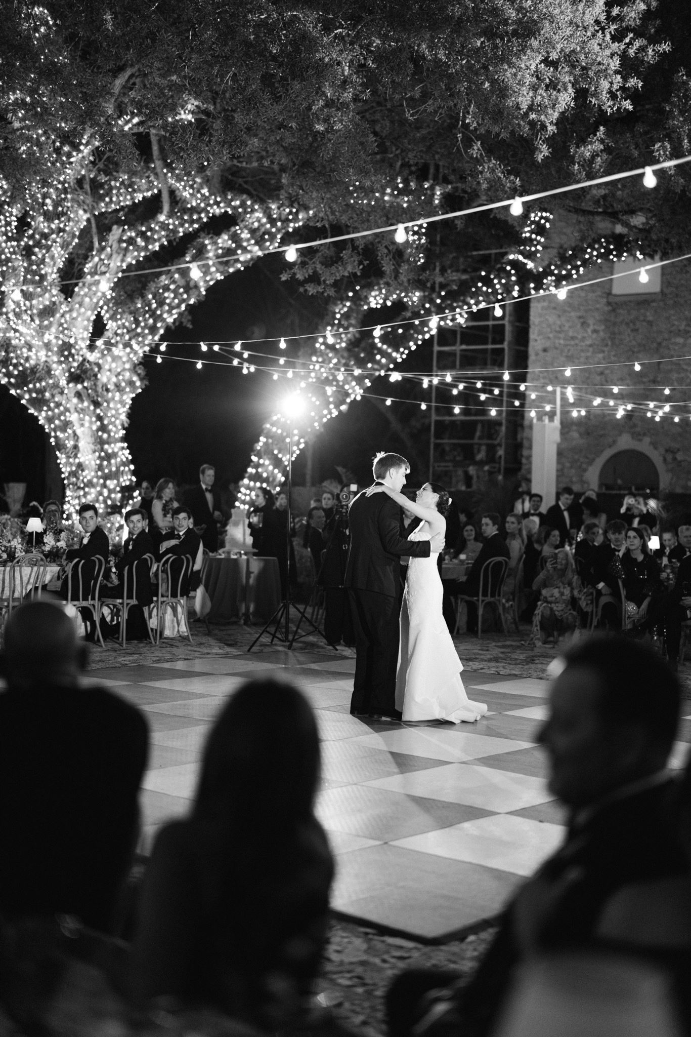 Ashley and Luke dancing under oak trees wrapped in lights in black and white