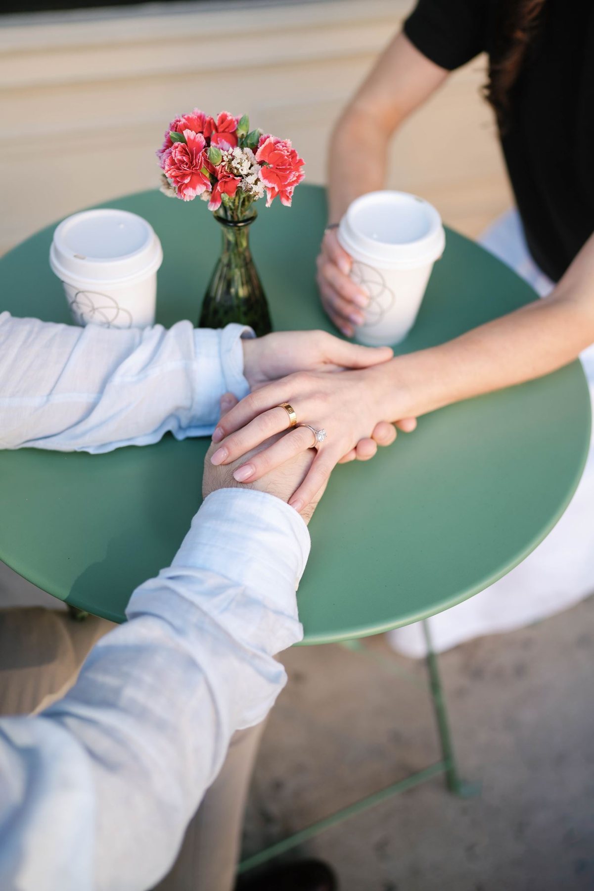Haley and Jeremy holding hands over a café table, her engagement ring visible