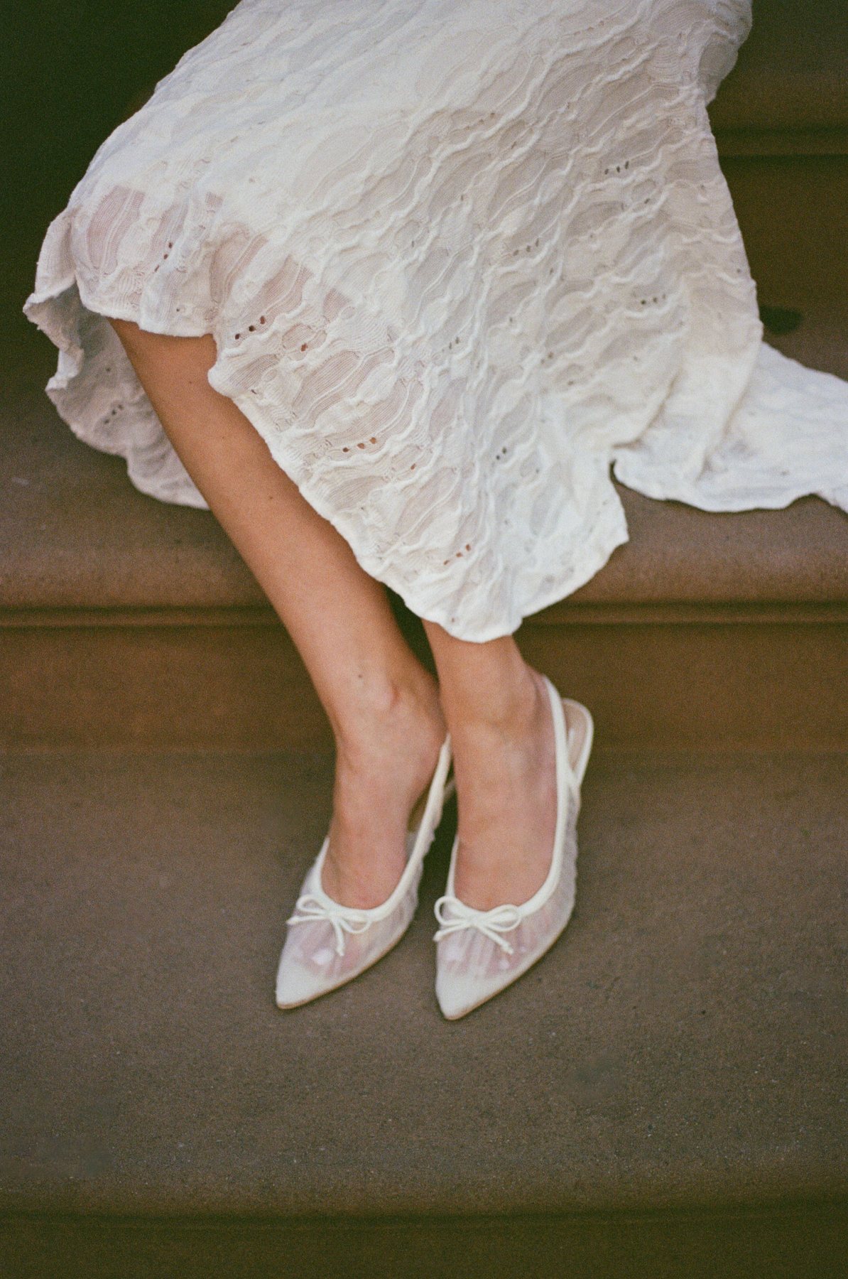 Film close-up of Haley's white eyelet dress and delicate white heels on a brownstone step