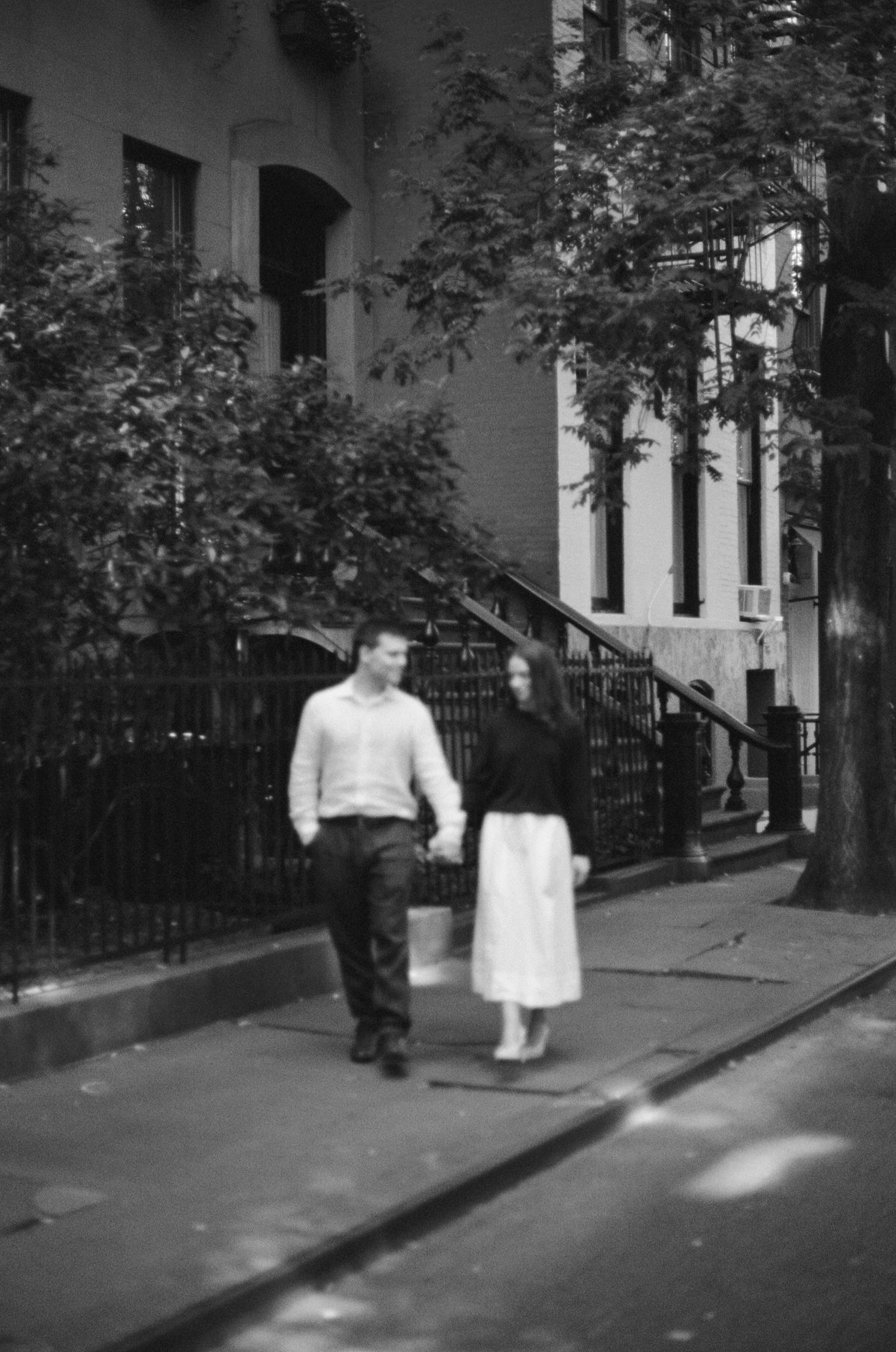 Black and white film photo of Haley and Jeremy walking down a tree-lined street in the West Village