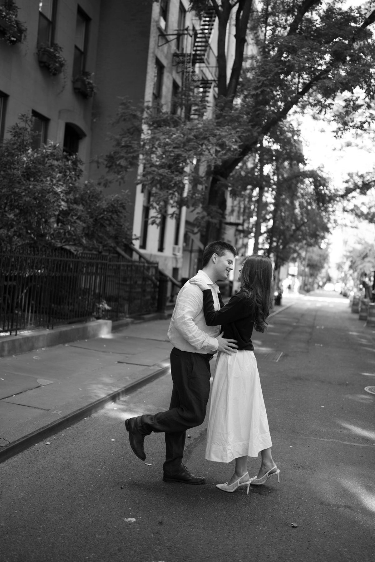 Black and white photo of Haley kicking up her heel as Jeremy kisses her on a West Village street